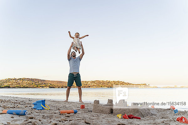 Sandburg und glücklicher Vater  der seine Tochter am Strand hochhebt