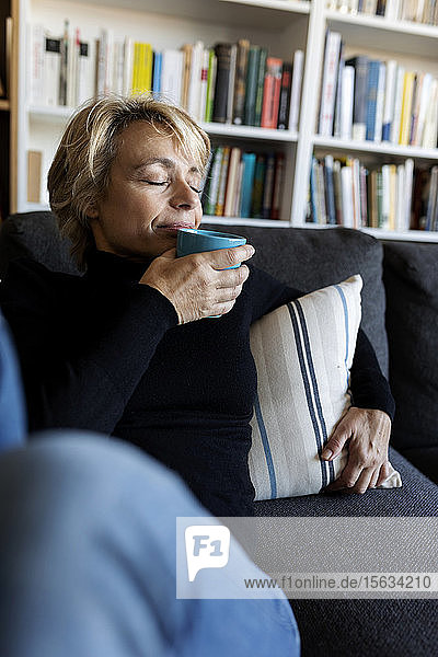 Reife Frau entspannt sich zu Hause auf der Couch und trinkt aus der Tasse
