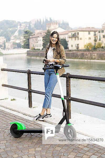 Young woman renting an e-scooter  holding her smartphone in Verona  Italy
