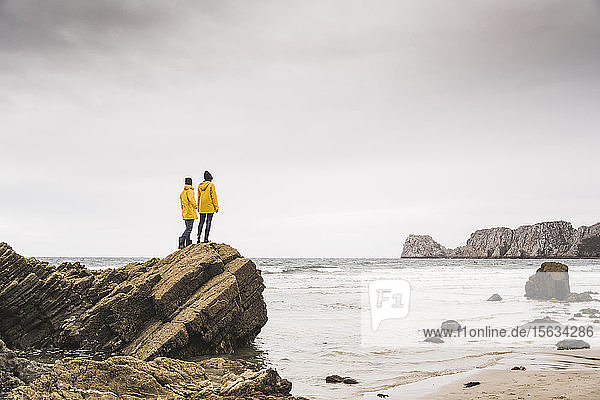 Junge Frau in gelben Regenjacken und auf einem Felsen am Strand stehend  Bretagne  Frankreich