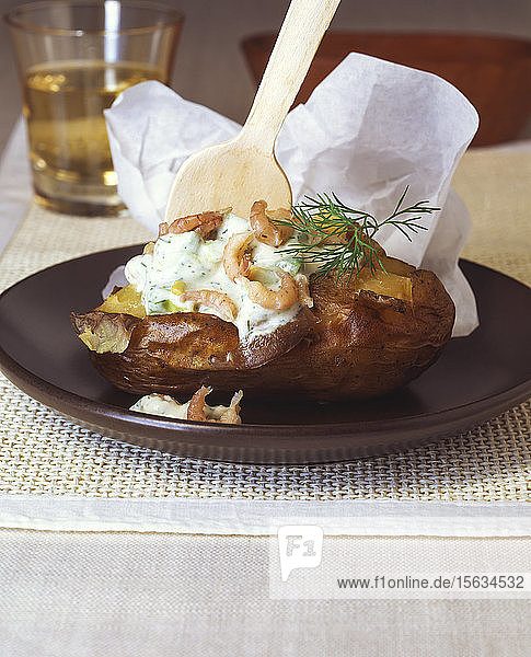Nahaufnahme einer Folienkartoffel mit Krabben und saurer Sahne  serviert in einem Teller auf dem Tisch