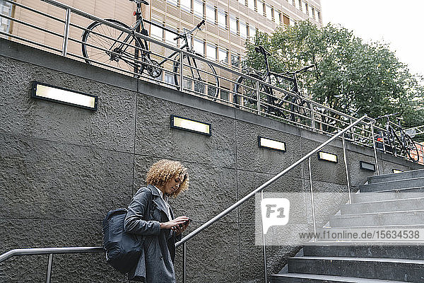 Frau mit Smartphone am Eingang einer U-Bahn-Station  Berlin  Deutschland