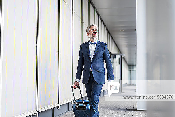 Mature businessman in a passageway with rolling suitcase on the go