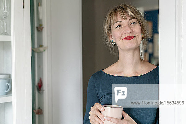 Porträt einer glücklichen Frau mit Tasse Kaffee zu Hause