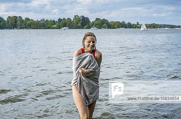 Lächelnde  in ein Handtuch gewickelte Frau steht in einem See