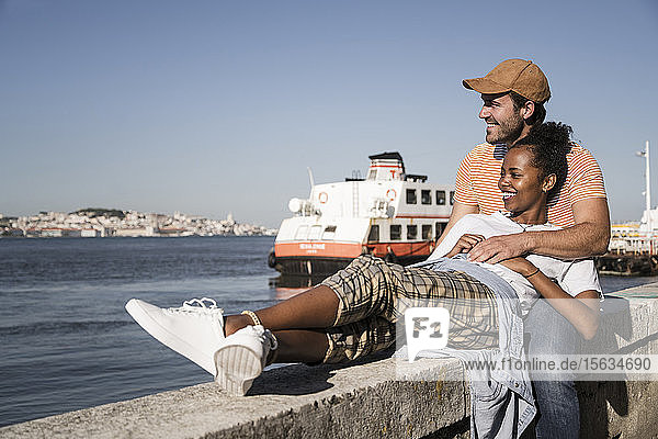 Glückliches junges Paar entspannt sich auf einer Mauer am Wasser Lissabon Portugal