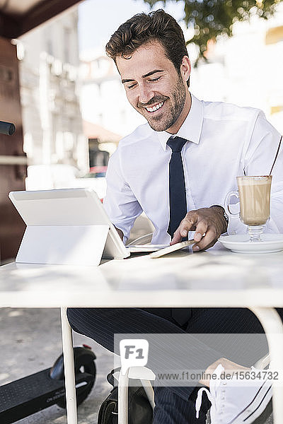 Lächelnder junger Geschäftsmann mit Tablet und Mobiltelefon in einem Café in der Stadt  Lissabon  Portugal