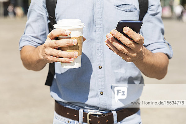 Nahaufnahme der Hände  die eine Tasse Kaffee und ein Smartphone halten