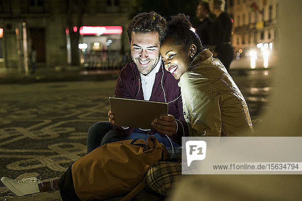 Porträt eines glücklichen jungen Paares  das sich Kopfhörer teilt und dabei ein digitales Tablet betrachtet  Lissabon  Portugal