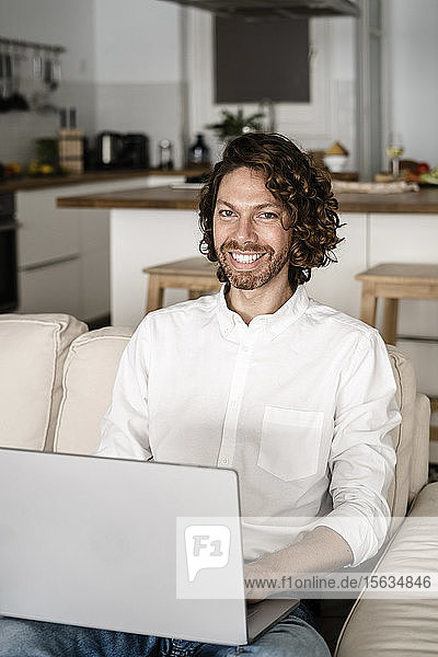 Porträt eines lächelnden Mannes mit Laptop auf der Couch zu Hause