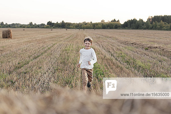 Smiling boy running over a stubble field