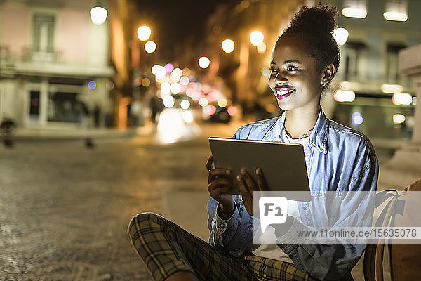 Porträt einer lächelnden jungen Frau mit digitalem Tablet in der Stadt bei Nacht  Lissabon  Portugal