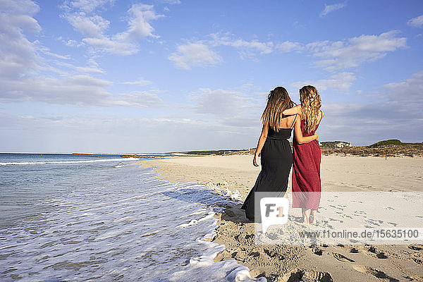 Two young women standing arm in arm on a beach