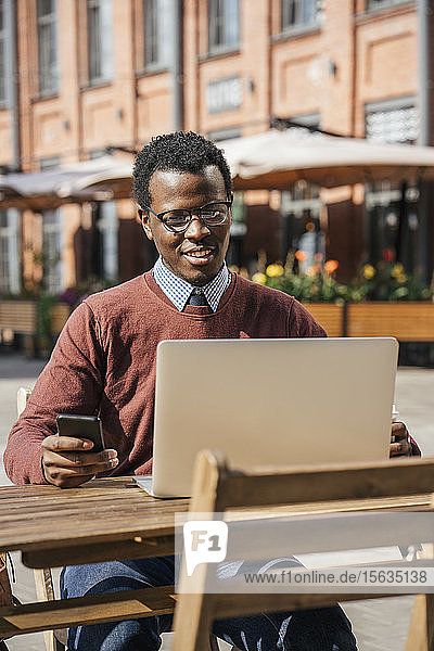 Junger Mann benutzt Smartphone und Laptop in einem Café