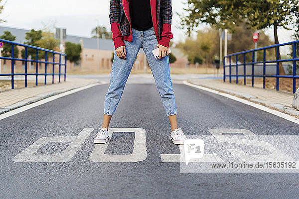 Crop view of young woman with mobile phone standing on the word 'stop' on the street