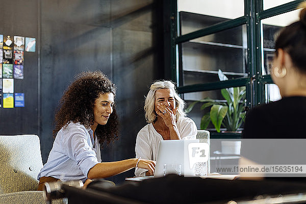 Fröhliche Geschäftsfrauen mit Laptop arbeiten zusammen im Loft-Büro