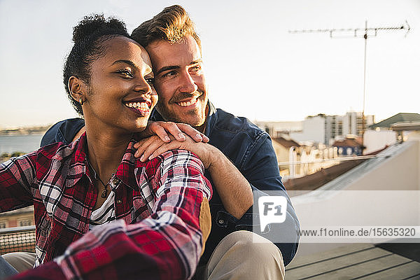 Happy affectionate young couple sitting on rooftop in the evening