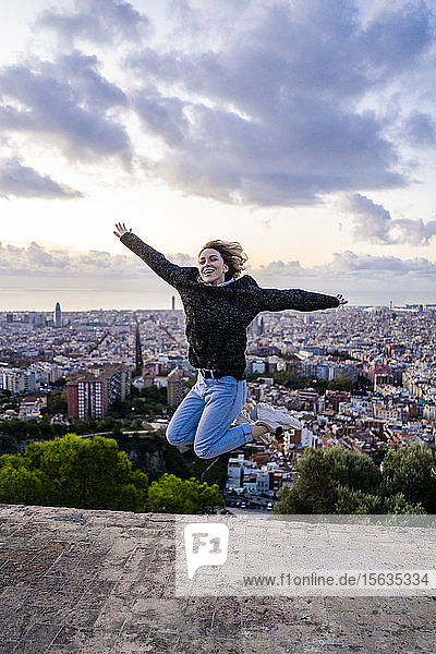 Unbeschwerte junge Frau springt bei Sonnenaufgang über die Stadt  Barcelona  Spanien