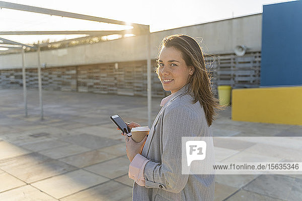 Porträt einer lächelnden jungen Frau mit Kaffee zum Mitnehmen und Mobiltelefon