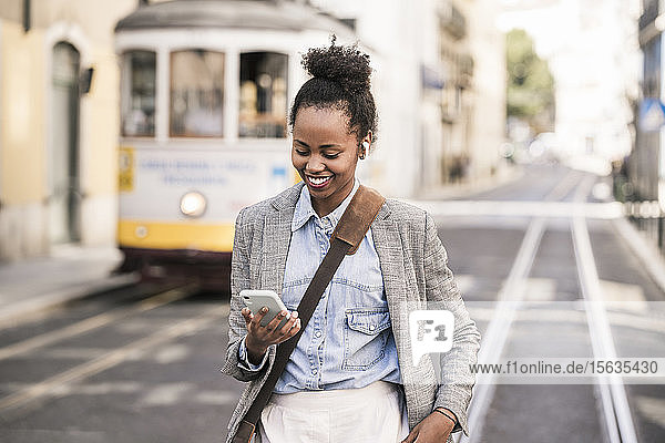 Smiling young woman with earphones and mobile phone in the city on the go  Lisbon  Portugal