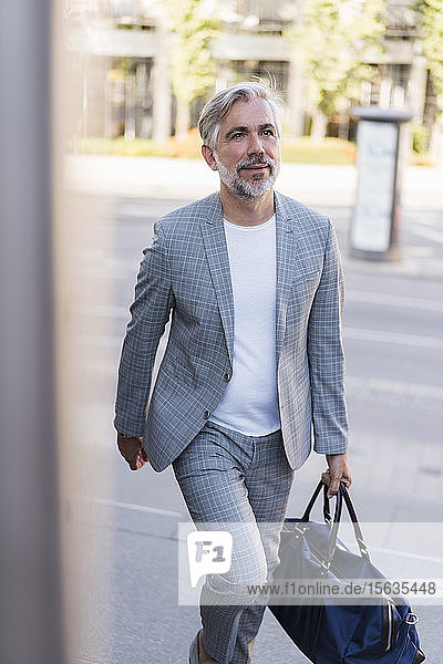 Fashionable mature businessman with travelling bag on the go in the city