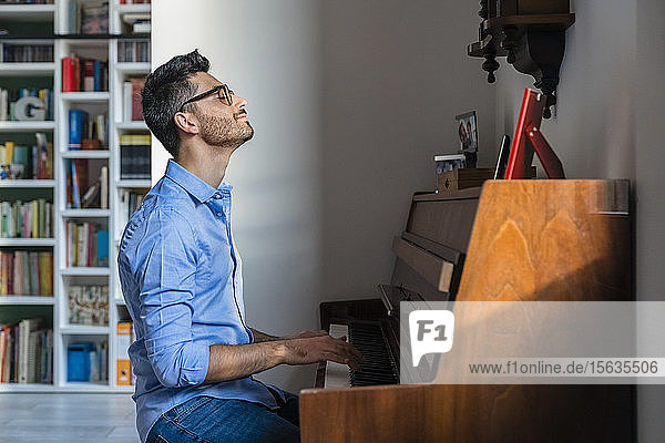 Lächelnder junger Mann mit geschlossenen Augen spielt zu Hause Klavier