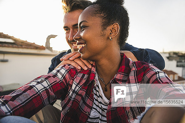 Happy affectionate young couple sitting on rooftop in the evening
