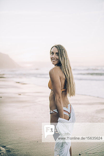 Young blond woman wearing bikini at the beach during sunrise