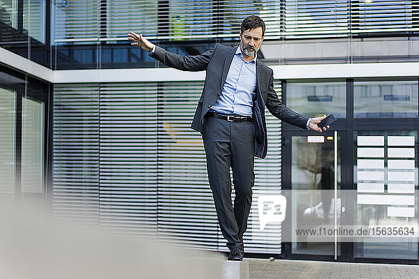 Ein reifer Geschäftsmann balanciert auf einer Wand vor einem Bürogebäude
