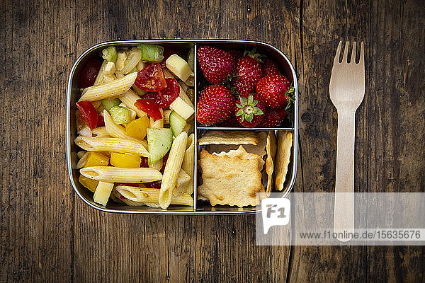 Direkt über Schuss Nudeln mit Erdbeeren und Crackern in Lunchbox auf Holztisch