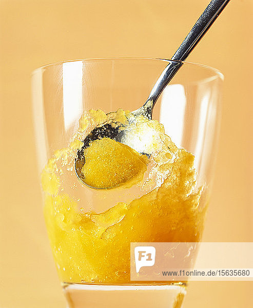 Mango-Fruchteis-Sorbet im Trinkglas vor orangem Hintergrund