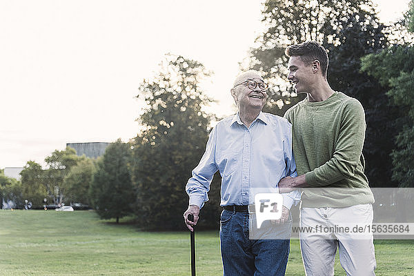 Junger Mann hilft seinem Großvater beim Spazierengehen im Park