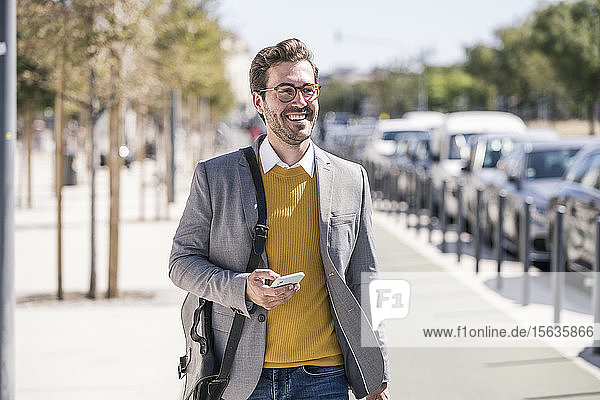 Lächelnder junger Geschäftsmann mit Handy in der Stadt unterwegs