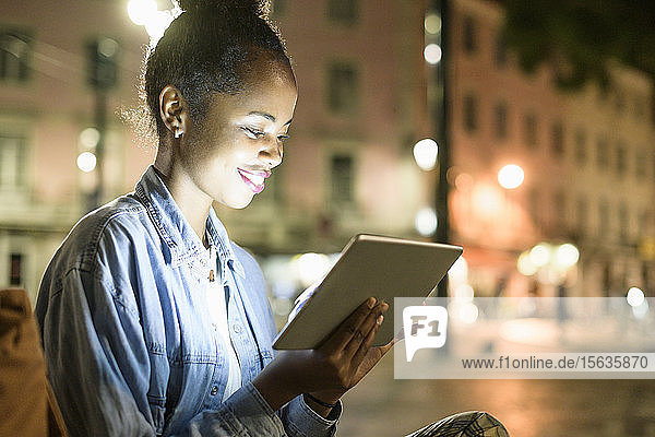 Lächelnde junge Frau mit digitalem Tablet in der Stadt bei Nacht  Lissabon  Portugal