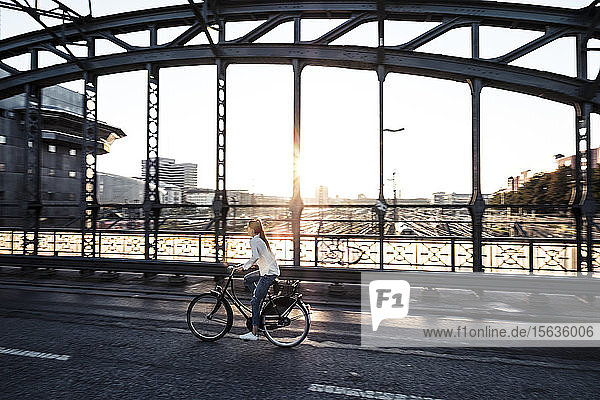 Junger Radfahrer auf einer Brücke bei Sonnenuntergang