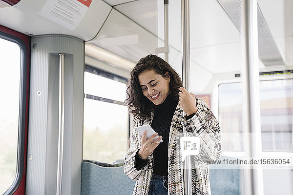 Lächelnde junge Frau mit Smartphone in der U-Bahn
