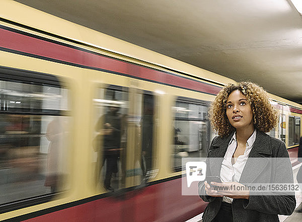 Frau mit Handy in der U-Bahn-Station  als der Zug einfährt