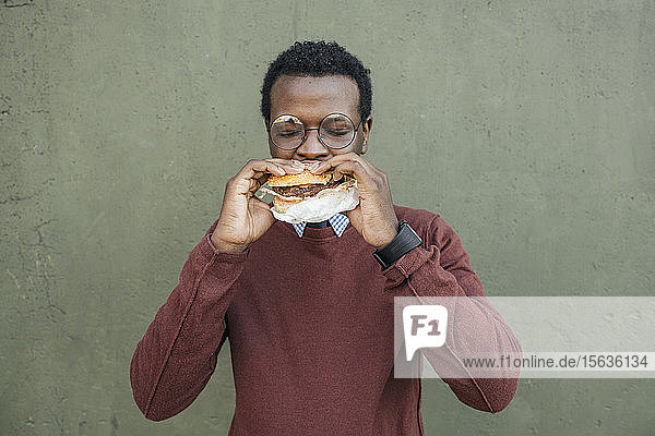 Junger Mann isst Cheeseburger  mit geschlossenen Augen
