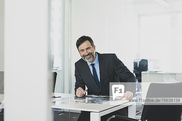 Porträt eines lächelnden reifen Geschäftsmannes  der im Büro am Schreibtisch sitzt