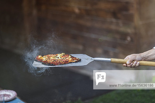 Abgehackte Hand einer Person  die auf einem Sommerfest gedämpfte Pizza mit Spachtel hält