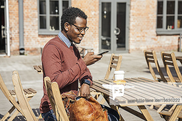 Junger Mann fotografiert seinen Cheeseburger mit seinem Smartphone