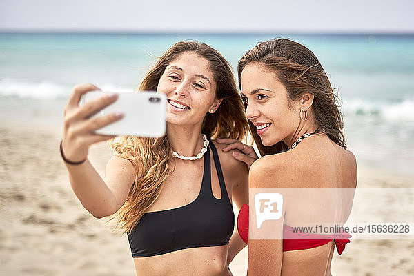 Zwei lächelnde junge Frauen beim Selfie am Strand