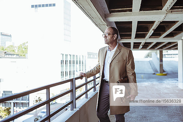 Mature businessman with briefcase standing on parking deck