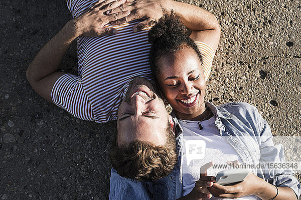 Happy young couple lying on concrete floor using cell phone