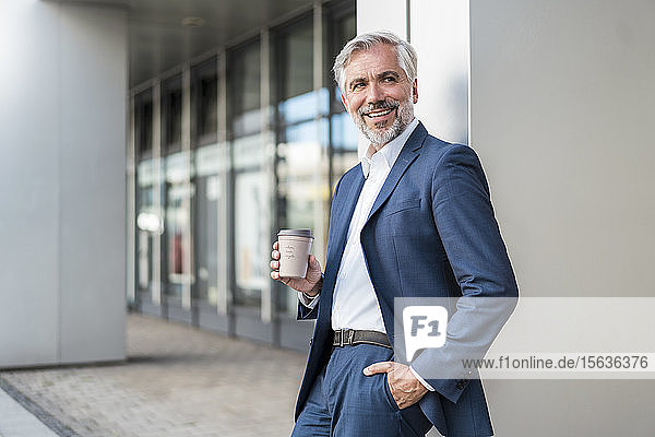 Lächelnder reifer Geschäftsmann mit Kaffee zum Mitnehmen in der Stadt