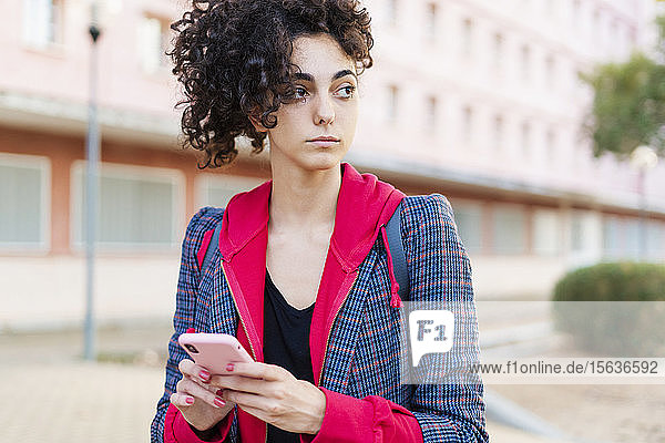 Porträt einer jungen Frau mit Mobiltelefon  die in die Ferne schaut
