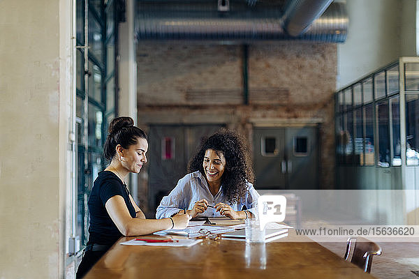 Two young businesswomen talking at conference table in loft office