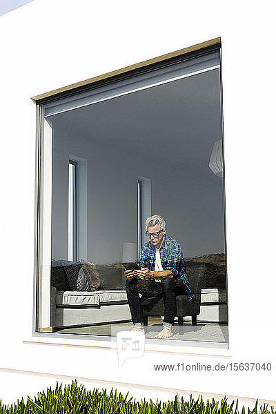 Lässiger Geschäftsmann sitzt in modernem Haus und schaut auf die Tafel