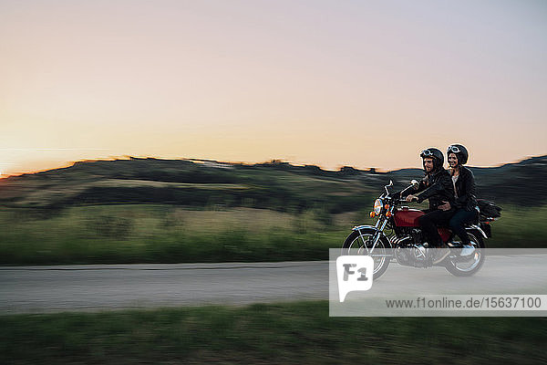 Junges Paar mit einem Oldtimer-Motorrad auf einer Landstraße bei Sonnenuntergang  Toskana  Italien
