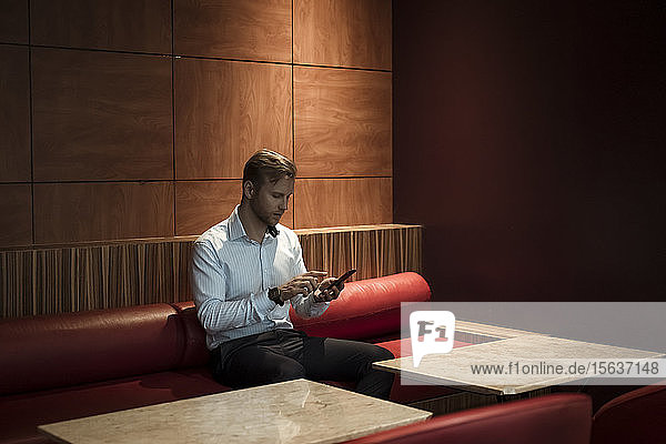 Geschäftsmann  der in einer Lounge sitzt und ein Smartphone benutzt
